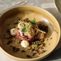 En konstnärlig råbiff med kapris, ägg och örter, serverad i en rustik skål. En kulinarisk upplevelse från Fjelie vingård.
