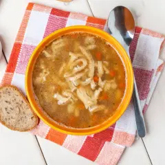 Pyszne flaki Ani gotuje, podane w pomarańczowej misce z chlebem i łyżką.
