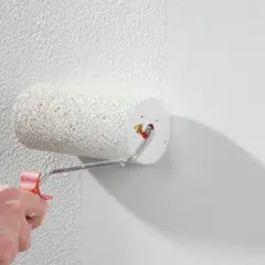 Eine Hand rollt mit einem Farbroller eine strukturierte Wand. Der Rollputz innen wird aufgetragen und verleiht der Oberfläche eine interessante Textur.
