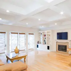 A spacious living room with a coffered ceiling featuring eight can lights. A large sectional sofa faces a fireplace and entertainment center.