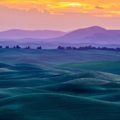 A fine art landscape photography captures rolling green hills under a vibrant sunset sky.