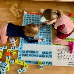 Dwie dziewczynki uczą się, jak nauczyć dziecko składać litery w wyraz, bawiąc się klockami z literami i planszą.