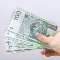 Dłoń trzyma stos banknotów 100 zł. To może być pomocne przy składaniu wniosku o bon energetyczny 2026.