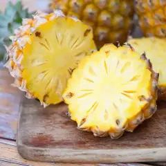 Dwa przekrojone ananasy na desce, jeden z nich wygląda jak ananas w ciąży, z widocznym wnętrzem i koroną.