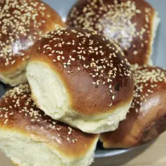 Pięć puszystych bułek do burgerów, posypanych sezamem, ułożonych na talerzu. Idealne na domowe burgery.