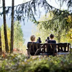 Två personer vilar på en bänk under en **weekend vandring i Sverige**. Höstfärger och solljus lyser upp skogen.