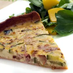 Rebanada de quiche de calabacín y bacon, con trozos de queso y una ensalada verde al lado.