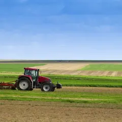 Tracteur rouge travaillant dans un champ, préparant le sol pour le semis direct. Paysage agricole sous un ciel bleu.
