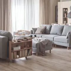 Przytulny salon inspiracje: szara sofa, drewniane meble, jasne zasłony i dekoracje tworzą ciepłą atmosferę.