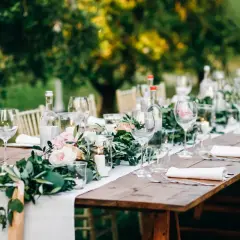 Tavola apparecchiata all'aperto con candele, fiori e bicchieri. Un esempio di addobbi tavoli matrimonio fai da te, con un tocco rustico ed elegante.