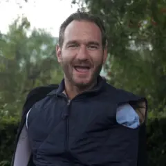 Nick Vujicic, lächelnd und mit offenem Mund, trägt eine blaue Weste über einem Hemd.