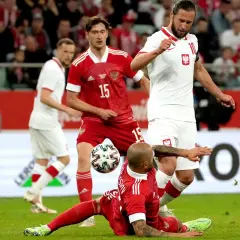 Piłkarze Polski i Rosji walczą o piłkę na boisku. Jeden z graczy Rosji leży na trawie, podczas gdy Polacy próbują przejąć kontrolę.