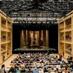 Widownia i scena w nowoczesnym teatrze królewskim w starej oranżerii. Drewniane galerie otaczają salę, a widownia zajmuje miejsca przed sceną.