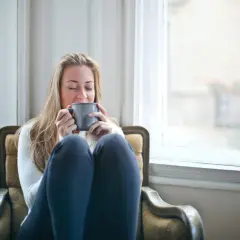 Kobieta z kubkiem w dłoniach, zamyślona, jakby rozważała różne nurty psychoterapii.