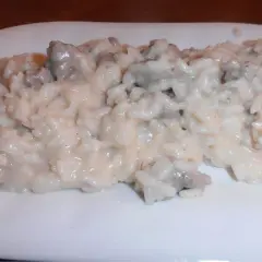 Un cremoso risotto salsiccia e patate, servito su un piatto bianco.