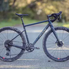 A dark blue Juliana gravel bike with gold lettering sits on a paved path, ready for adventure.