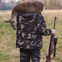 Myśliwy w kamuflażu niesie na ramieniu upolowanego sarnę, trzymając strzelbę. Czy myśliwy zawieszony może polować?