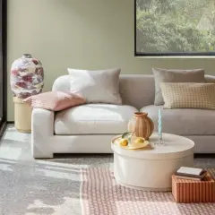 Gemütliches Wohnzimmer mit hellgrauem Sofa, Kissen in sanften sommer farben und einem runden Couchtisch.