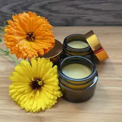 Zwei Gläser mit selbstgemachter Ringelblumensalbe, daneben leuchtend orange und gelbe Ringelblumen.