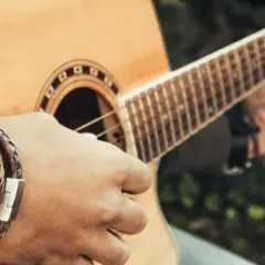 Dłoń grająca na gitarze, tworząca akord e moll. Na nadgarstku widać bransoletkę ze skóry.