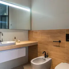 Bagno moderno con lavabo ovale, bidet e WC. Le pareti sono rivestite con piastrelle effetto legno e grigie, un mix che offre ottime opinioni per chi ama il design.