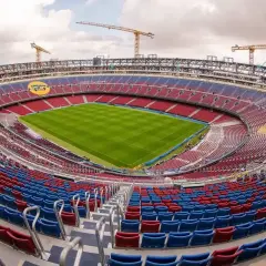 Widok na nowy stadion Barcelony w trakcie budowy. Żurawie górują nad trybunami w barwach klubu, a murawa lśni zielenią.
