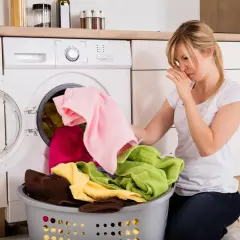 Donna con la mano sul naso vicino a una lavatrice che puzza di fogna. Rimedi per eliminare il cattivo odore.