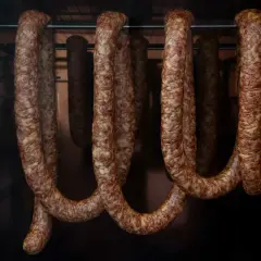 Wędzone kiełbasy wiszą w komorze wędzarniczej. Widać, że popełniono błędy podczas wędzenia, bo niektóre są nierówno uwędzone.