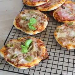 Mini pizze z tuńczykiem i oliwkami, idealne, gdy zastanawiasz się, jak zrobić pizzę. Na ruszcie stygną pyszne, domowe wypieki.