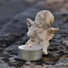 Aniołek czuwa przy płonącej świecy, symbolizując pamięć i żal po śmierci bliskiej osoby.