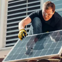 Mężczyzna w okularach ochronnych montuje panel słoneczny na dachu, walcząc ze zmianami klimatycznymi.