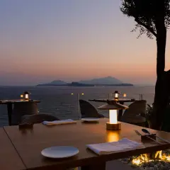 Tavoli apparecchiati con vista mare al tramonto, un'atmosfera magica che fa pensare ai migliori ristoranti di Napoli.