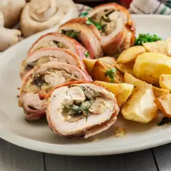 Roladki z kurczaka zawinięte w boczek, podane z pieczonymi ziemniakami i ziołami.