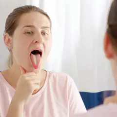 Mujer se mira en el espejo, mostrando su lengua blanca, preocupada por un posible dolor de garganta.