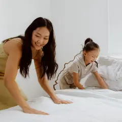Mutter und Kind machen das Bett frisch. Der Boxspringbett Topper wellt sich leicht, während sie die Bettwäsche glattziehen.
