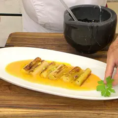 Puerros a la plancha, dorados y tiernos, servidos en una salsa anaranjada y decorados con perejil fresco.
