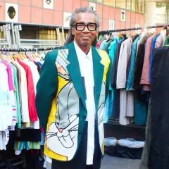 Man in a Bugs Bunny jacket stands by racks of colorful clothes, a testament to creative clothes upcycling.