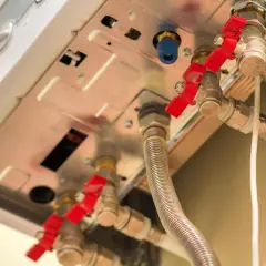 Dettaglio di valvole rosse e tubi di una caldaia, utili per capire come abbassare pressione.