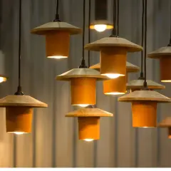 Un grupo de lámparas colgantes de diseño moderno, con pantallas de madera y cilindros naranjas, iluminan el espacio.