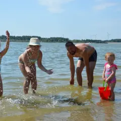 Rodzina pluska się w wodzie na zalewie Cieszanowice. Dzieci radośnie chlapią, a ojciec dogląda zabawy.