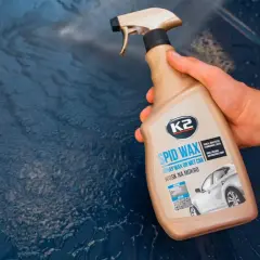Dłoń trzyma butelkę z woskiem w sprayu K2 SPID WAX, gotową do usunięcia dziwnych plam na lakierze samochodowym.