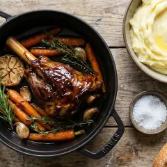 Souris d'agneau au four, caramélisée et tendre, servie avec des carottes rôties, de l'ail confit et du romarin. Accompagnée de purée de pommes de terre et de gros sel.