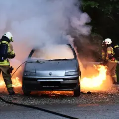 Strażacy walczą z płomieniami, gasząc samochód, który uległ samozapłonowi. Gęsty dym unosi się w powietrze.