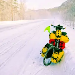 A fully loaded bicycle sits on a snowy road, a testament to adventure. The rider's concern about the brake fluid freezing point is evident in this winter scene.