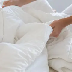 Hands smoothing a white duvet, a step in how to wash bedding for a fresh, clean sleep.
