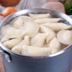 Gotowanie pierogów w garnku. Woda wrze, a pierogi unoszą się na powierzchni. W tle widać olej i koperek. Dowiedz się, ile gotować pierogi, by były idealne.