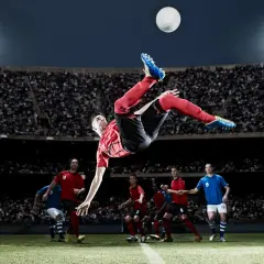 Piłkarz wykonuje przewrotkę na tle stadionu pełnego kibiców.