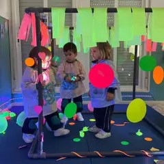 Niños explorando un aula multisensorial infantil con luces de neón, globos y elementos interactivos.