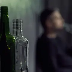 Puste butelki, jedna z nich jest przezroczysta, a obok niewyraźna postać pije alkohol. To może być jego dawka śmiertelna.