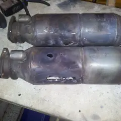 Dos catalizadores de coche rotos, con agujeros visibles, evidencian porque se rompe el catalizador del coche por sobrecalentamiento o golpes.